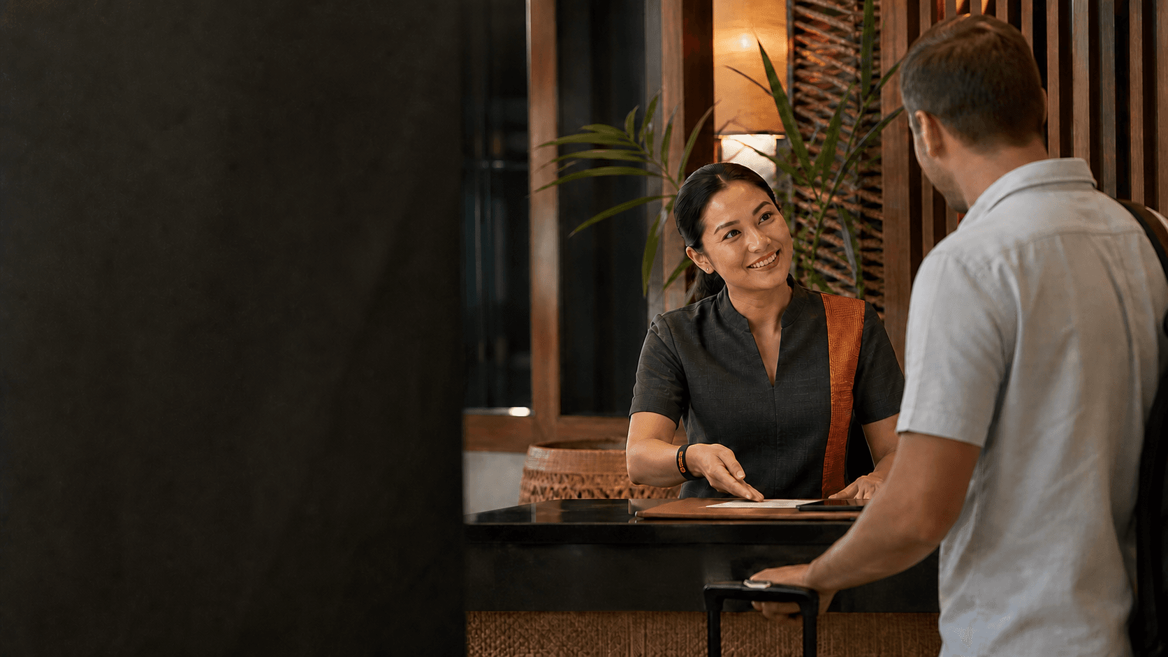 A Filipino hotel front-desk professional wearing a Grate band and helping an arriving guest